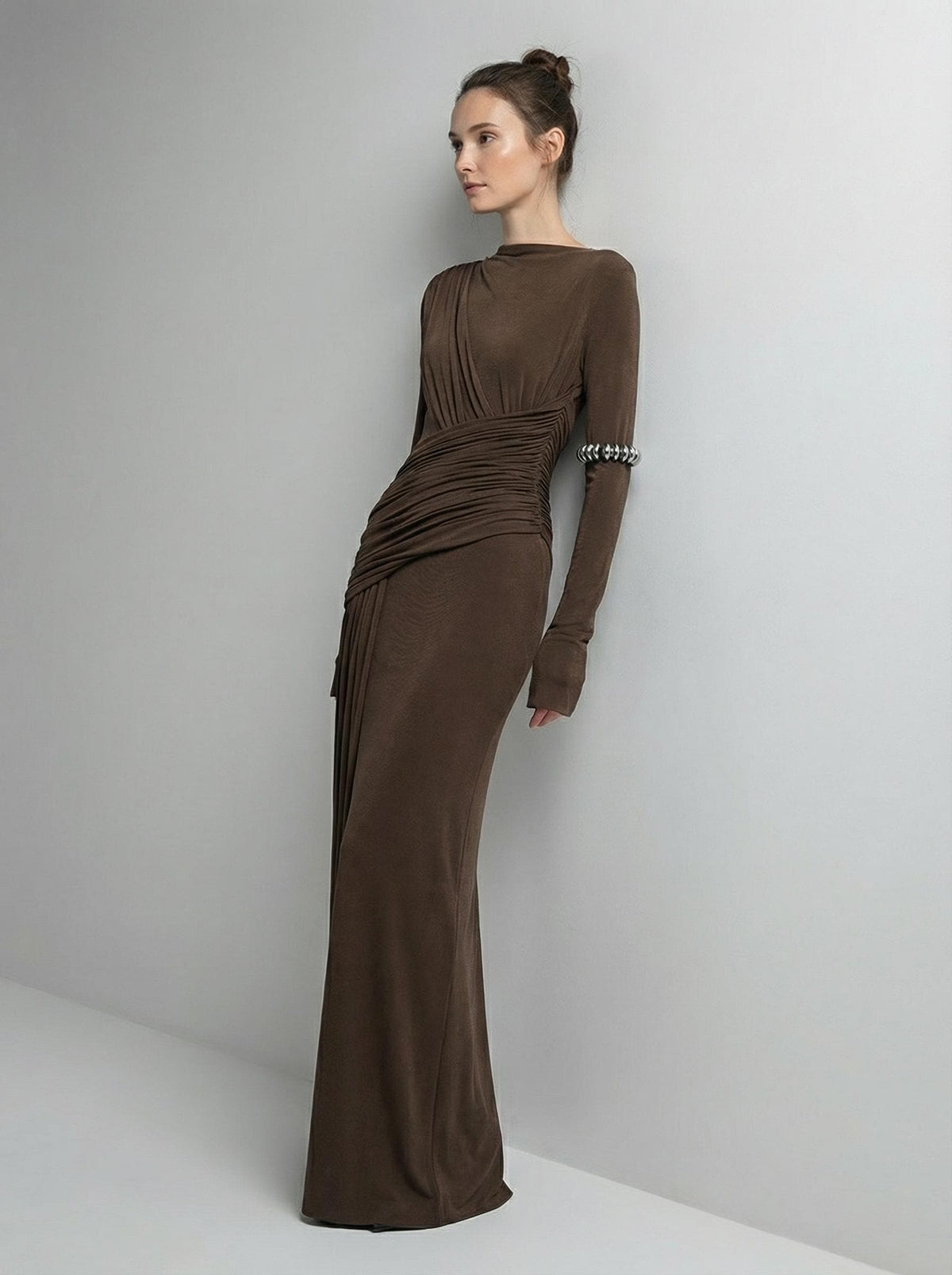 Brown high-neck maxi gown from a three-quarter angle in a plain studio, showing the gathering at the shoulder and the ruched waist.