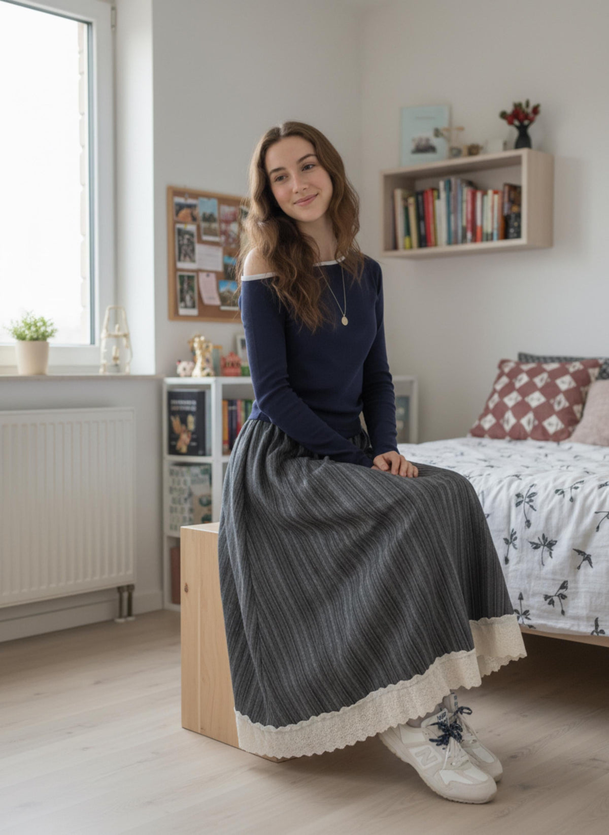 Front view of the Grey Striped midi skirt with a cream lace hem, worn with a navy long-sleeve top, seated on a wooden stool in a bedroom.