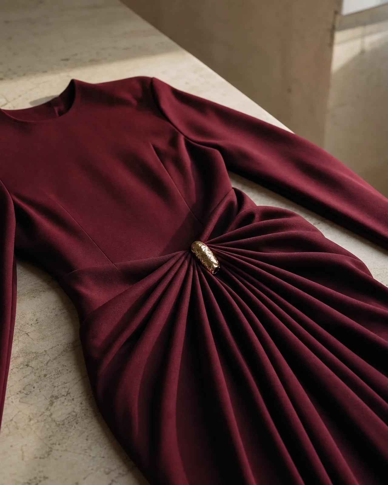 Saraura's burgundy draped gown laid flat, the sculpted gold ornament at the waist with pleats radiating from it.